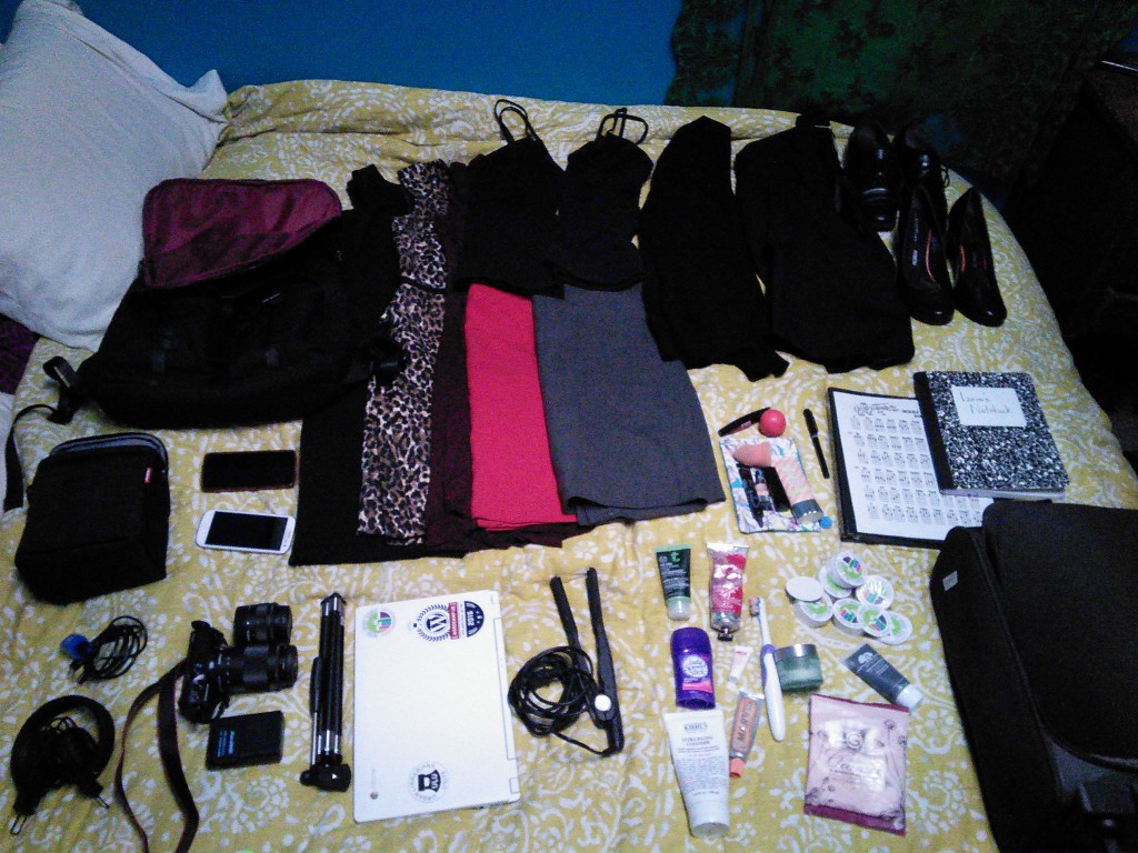 clothes and tech stuff laid out on a bed to be packed